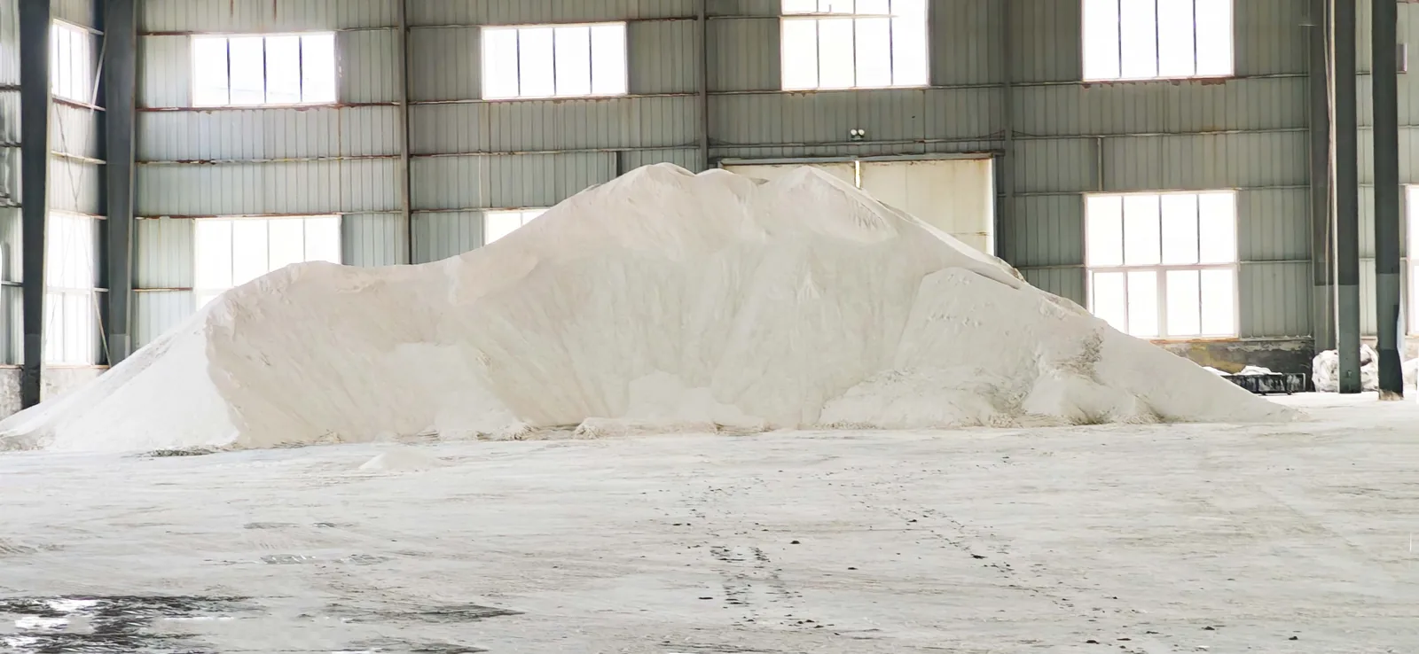 Large white bulk raw-material pile stored inside the plant warehouse